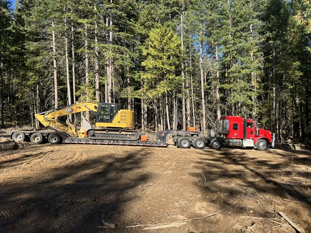 Bay Builders truck delivering an excavator to a job site